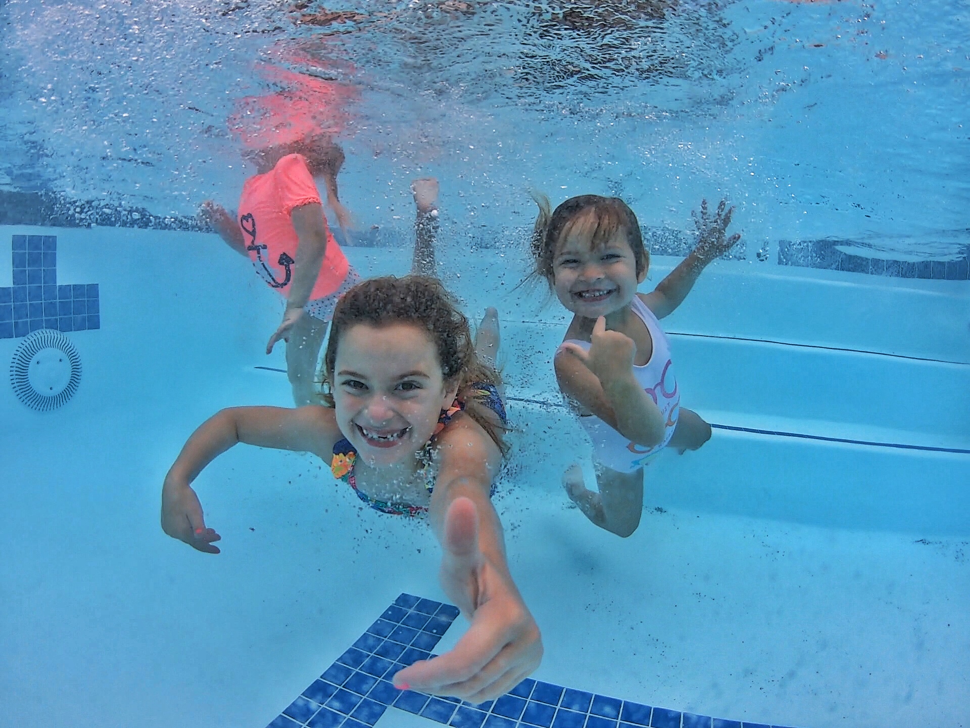 Three children swimming underwater and smiling during a Jump-Start swim lesson at Nova Swim School